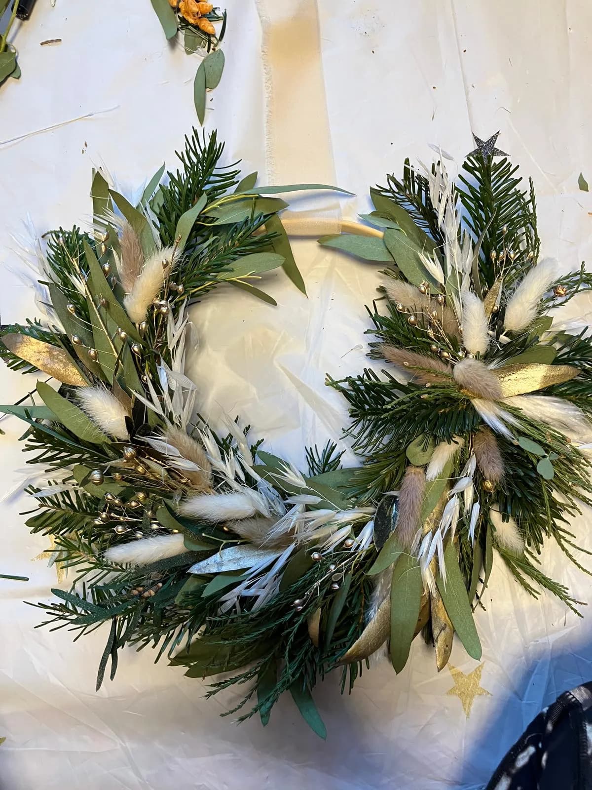 Ein Kranzreif mit getrocknetem Nadelgrün, Eukalyptus, Samtgras, weißem Hafer, goldenen Blättern und goldenen Beeren