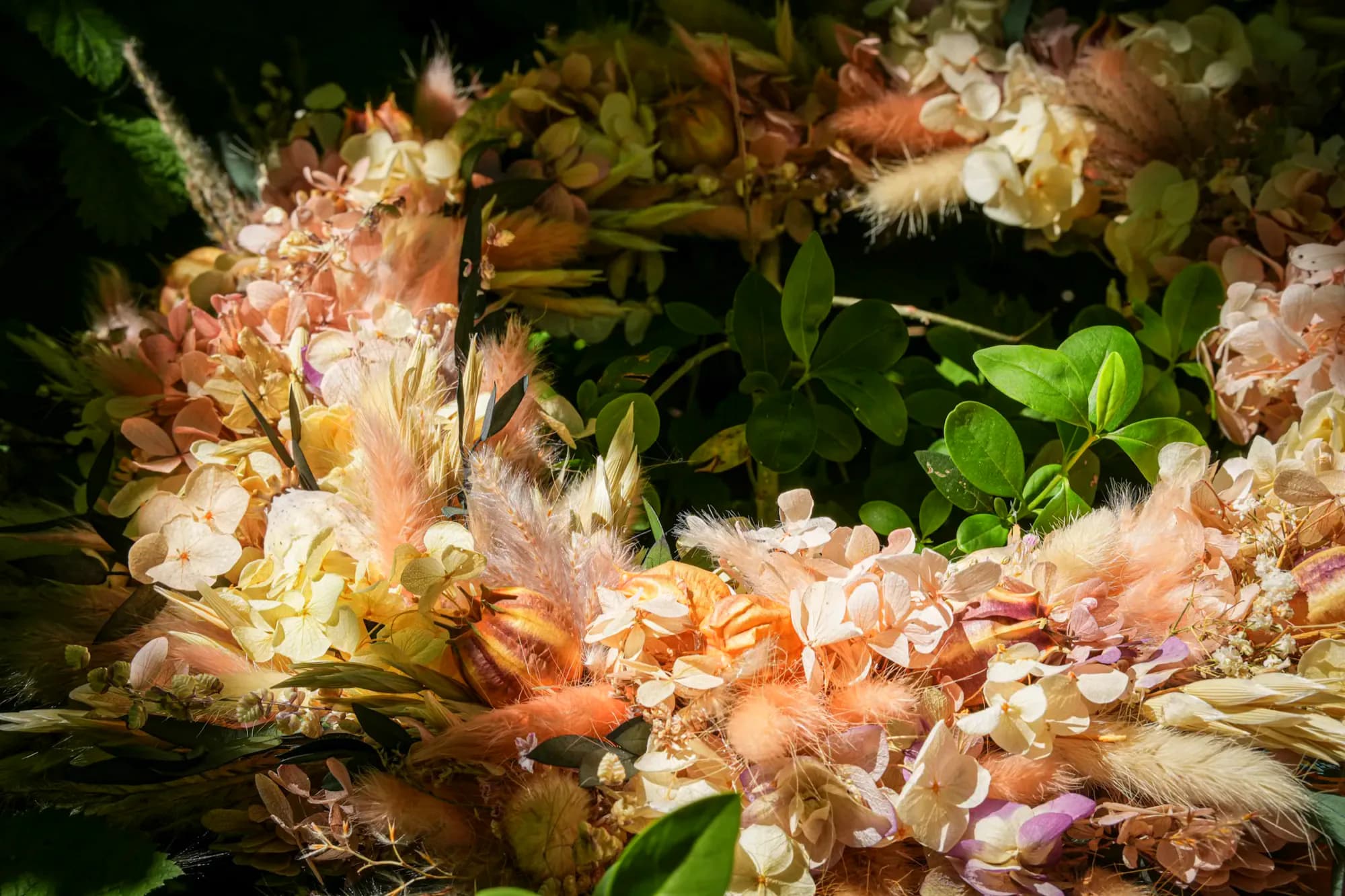 Nahaufnahme eines Kranzes: helle Trockenblüten in Creme und Altrosa zwischen dunklem Grün